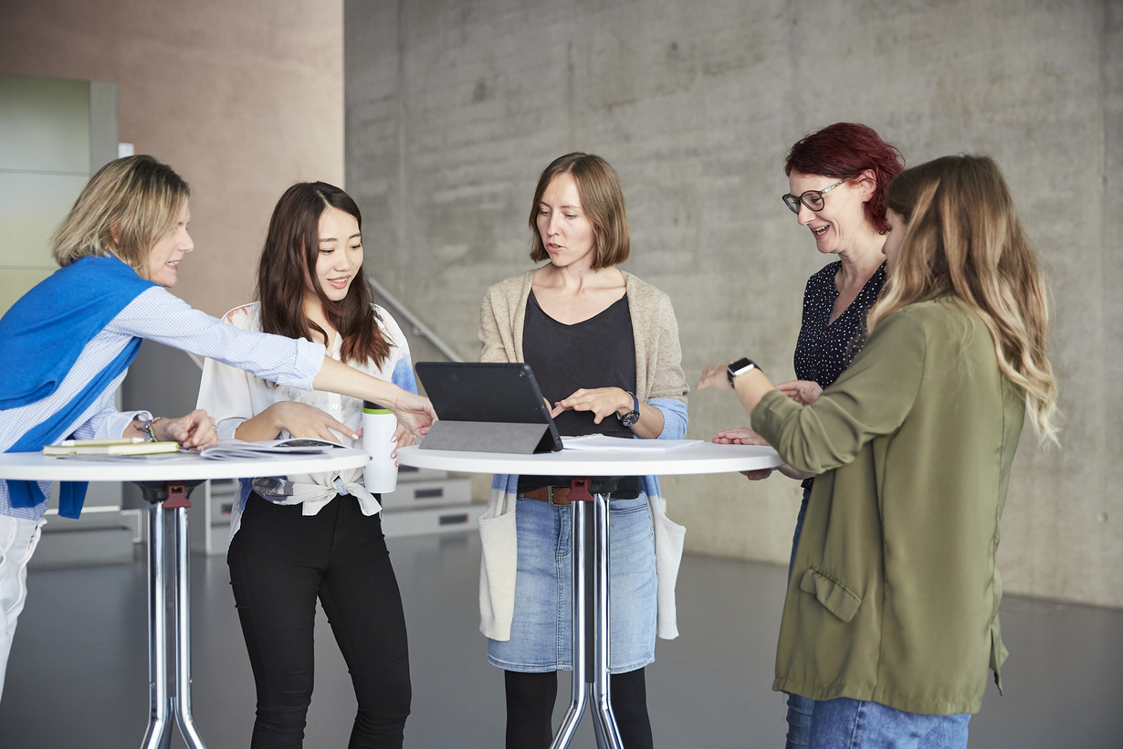 Fünf Frauen stehen am Tisch und diskutieren